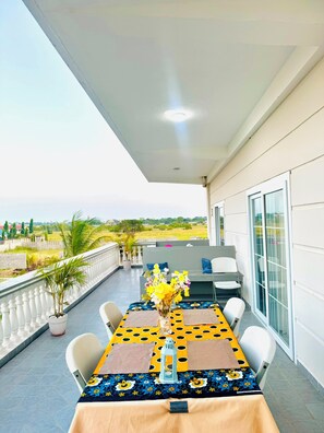A balcony with a table set for dining, chairs, a potted plant, and a view of the countryside. - Sunset Apartments Bagamoyo (Bagamoyo)