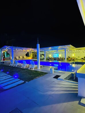 Zona de piscina exterior amb gandules i un bar.