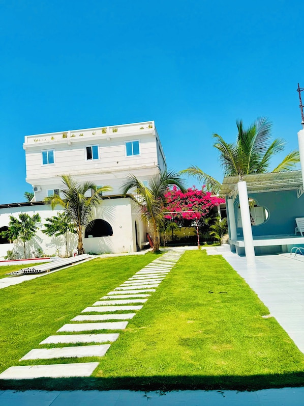 A modern building with a white exterior, a paved pathway leading to the entrance, and a well-maintained lawn.