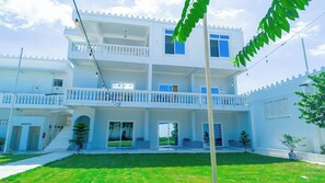 A multi-story building with a balcony, a staircase, and a well-maintained lawn. - Sunset Apartments Bagamoyo (Bagamoyo)