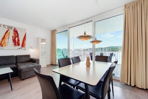 A modern hotel room with a dining area, a sofa, and a large window with a city view. - Promenadenvilla 23, Apartment 07 (Lübeck-Travemünde)