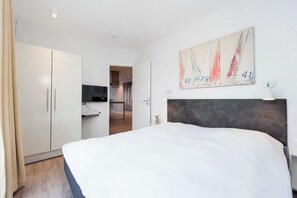 Quarto moderno com uma cama grande, um guarda-roupa, uma televisão e um quadro na parede.