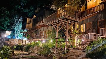 A multi-level wooden structure with outdoor stairs, surrounded by greenery and stone walls.