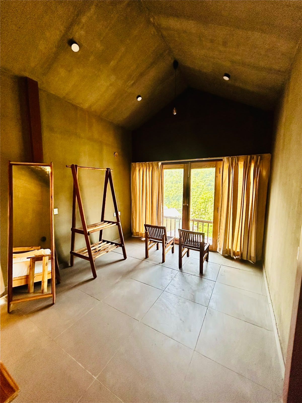A room with a high ceiling, a wooden ladder, a wooden bench, and a window with curtains.
