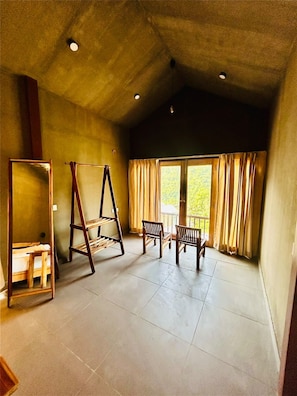 Une pièce avec un plafond haut, une échelle en bois, un banc en bois et une fenêtre avec des rideaux.