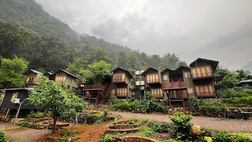 A cluster of wooden cabins with balconies, surrounded by lush greenery and a mountainous backdrop.