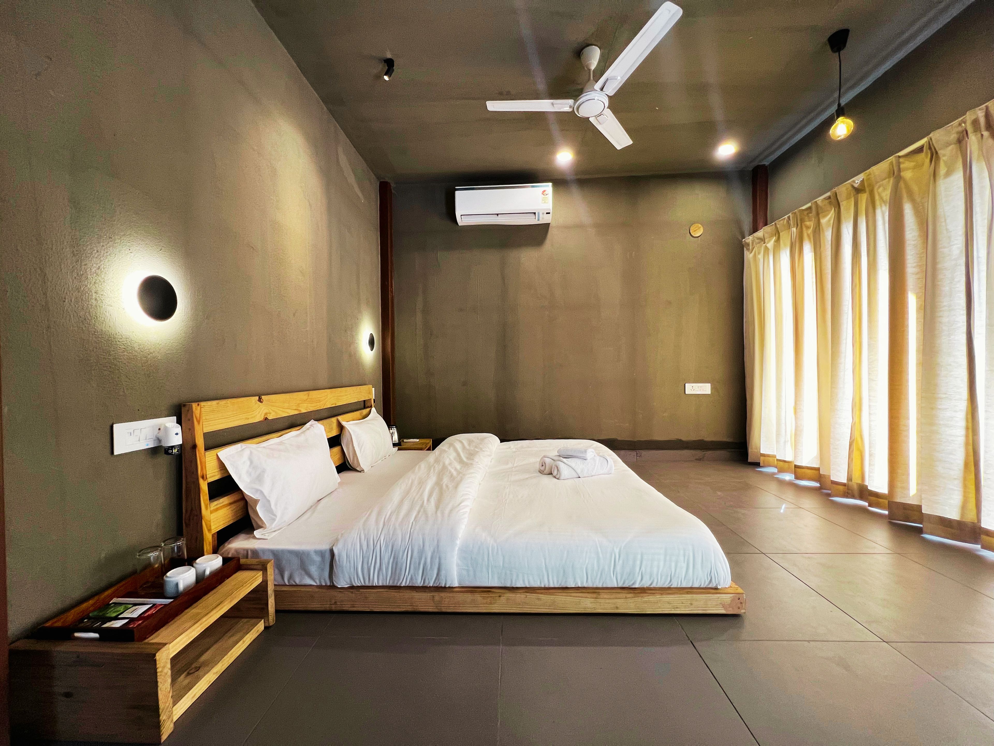 Una habitación de hotel con cama, ventilador de techo, equipo de aire acondicionado y ventana con cortinas.