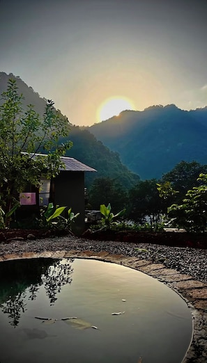 A tranquil outdoor setting with a small building, a pond, and a mountainous backdrop.
