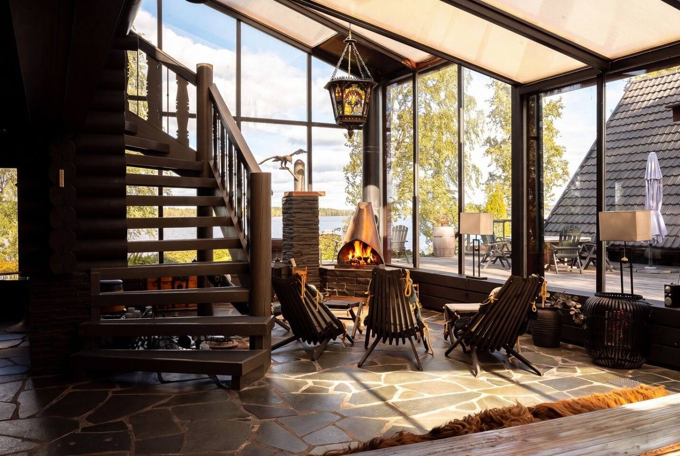 A stone-floored room with a fireplace, wooden chairs, and a staircase.
