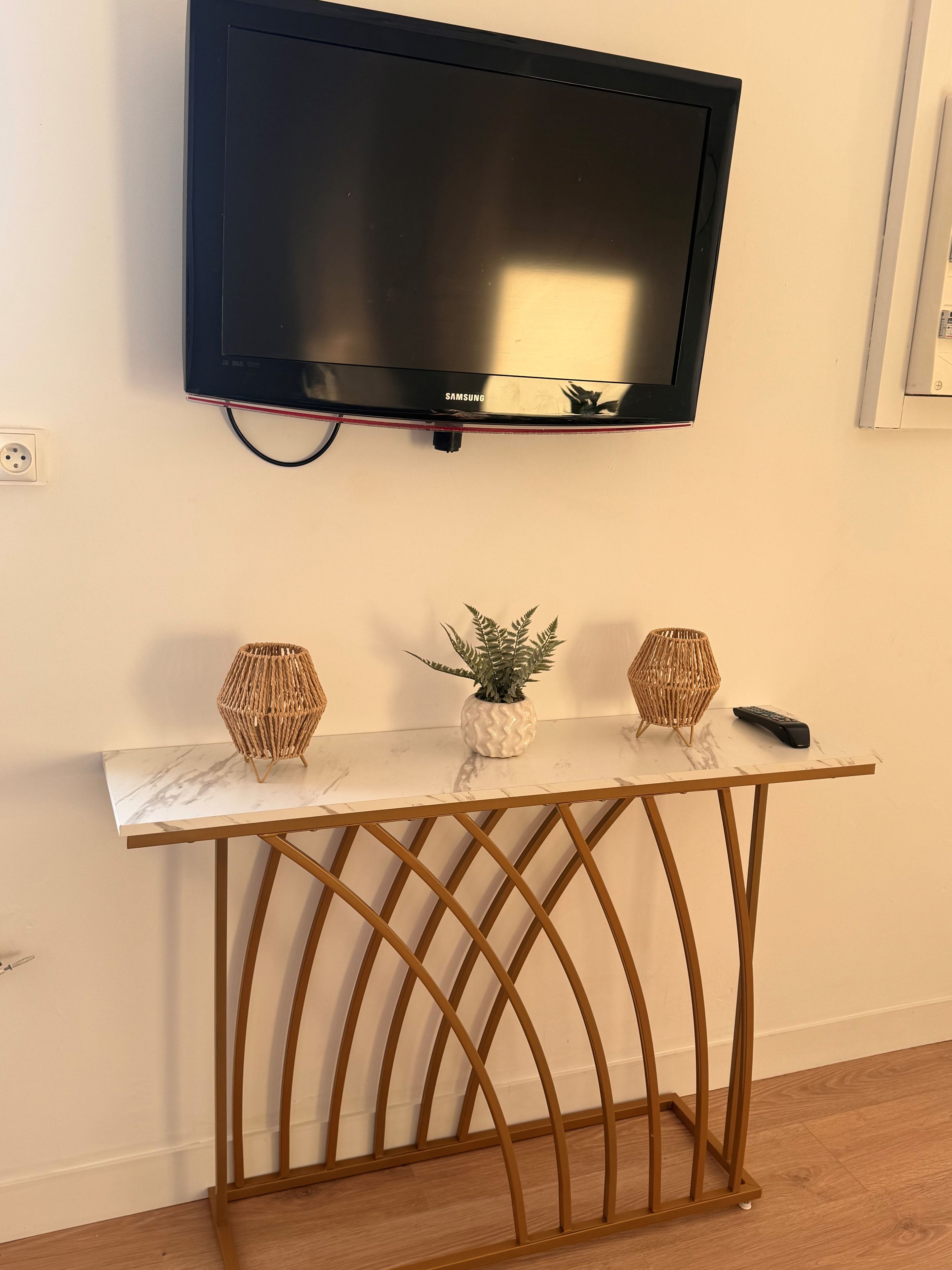 Een televisie bevestigd aan een muur boven een marmeren console tafel met twee decoratieve vazen en een klein plantje.