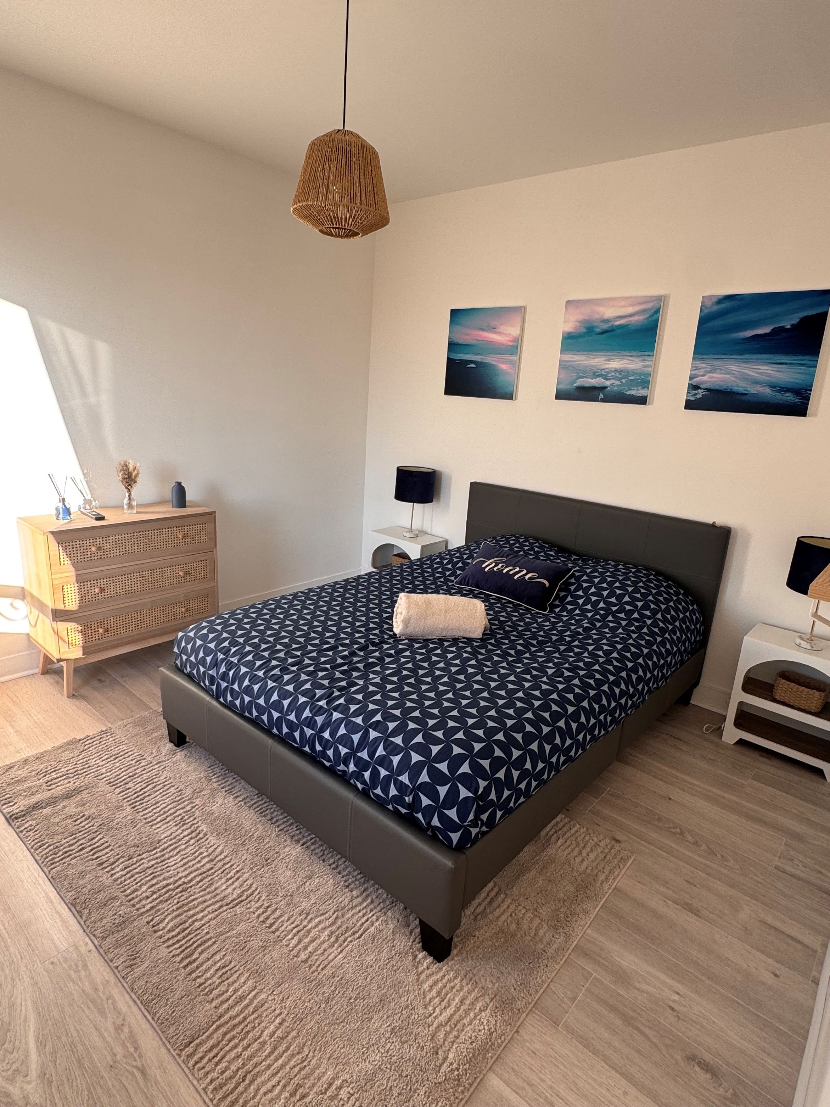 Een slaapkamer met een bed, nachtkastjes, een dressoir en wanddecoratie.