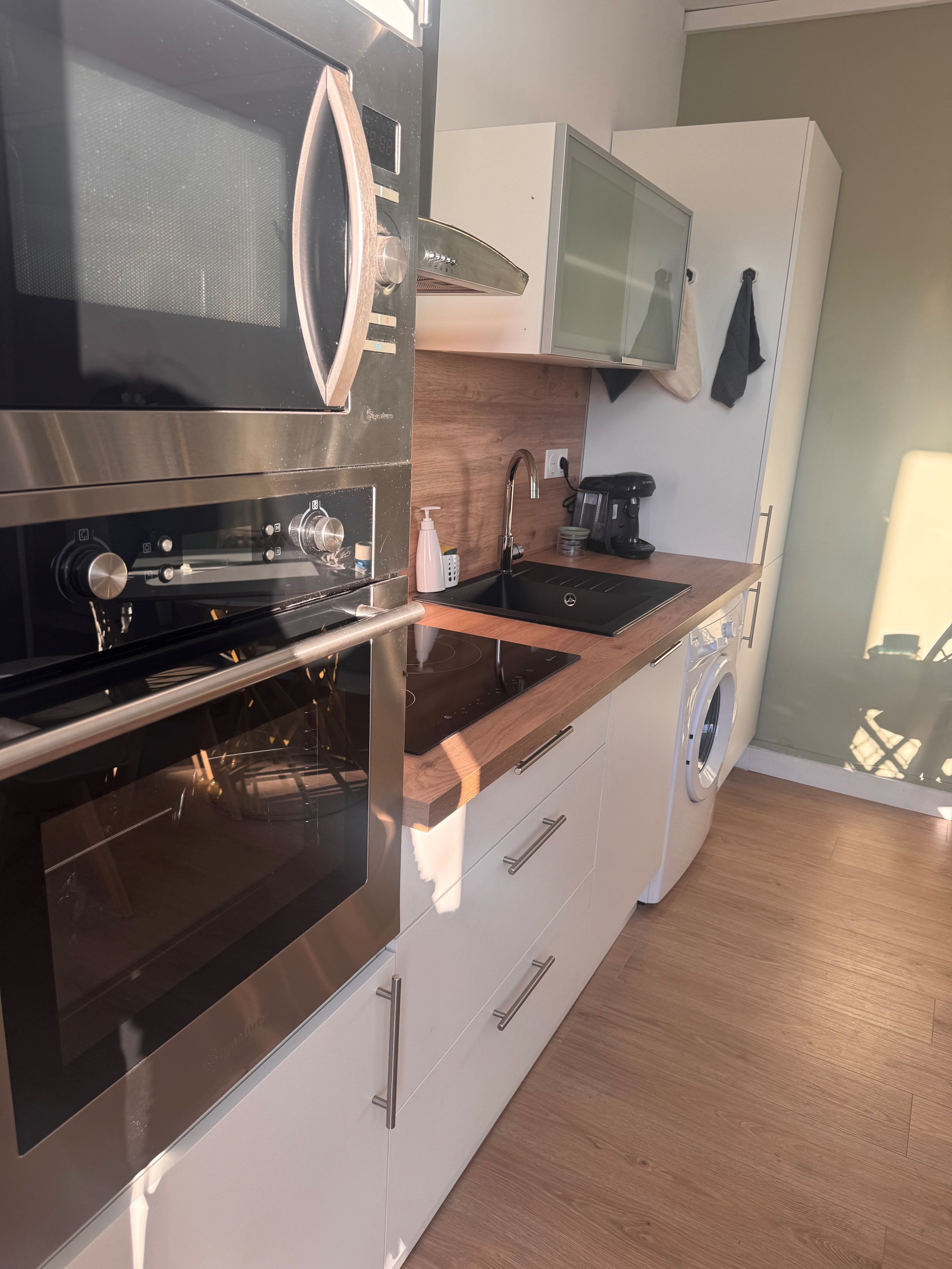 Une cuisine moderne dotée d’appareils électroménagers en acier inoxydable, d’un plan de travail en bois, d’un lave-linge encastré et d’un four à micro-ondes placé au-dessus de la cuisinière.