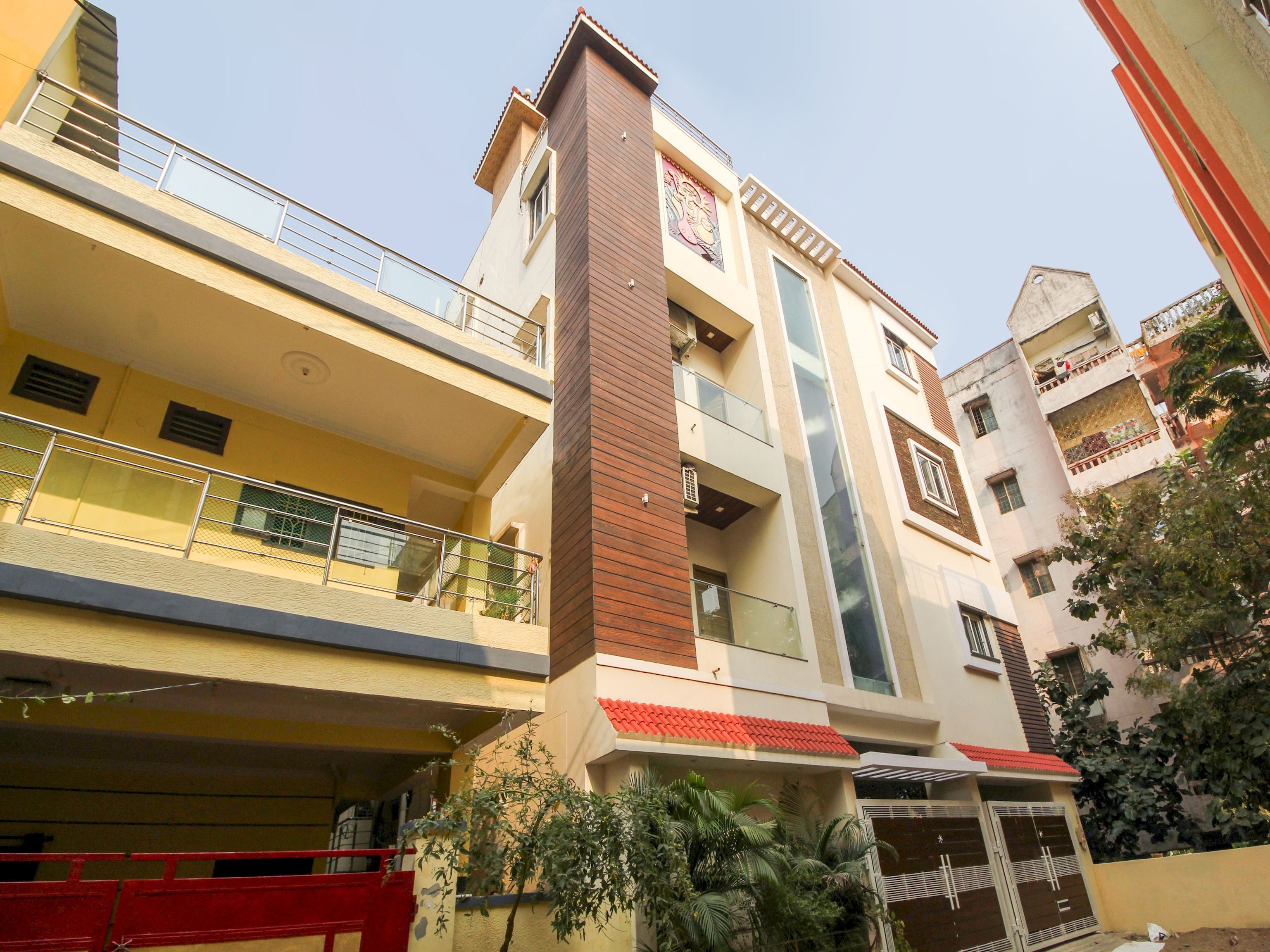 Un edificio residencial de varios pisos con balcones, un elemento vertical central y una entrada con techo rojo.