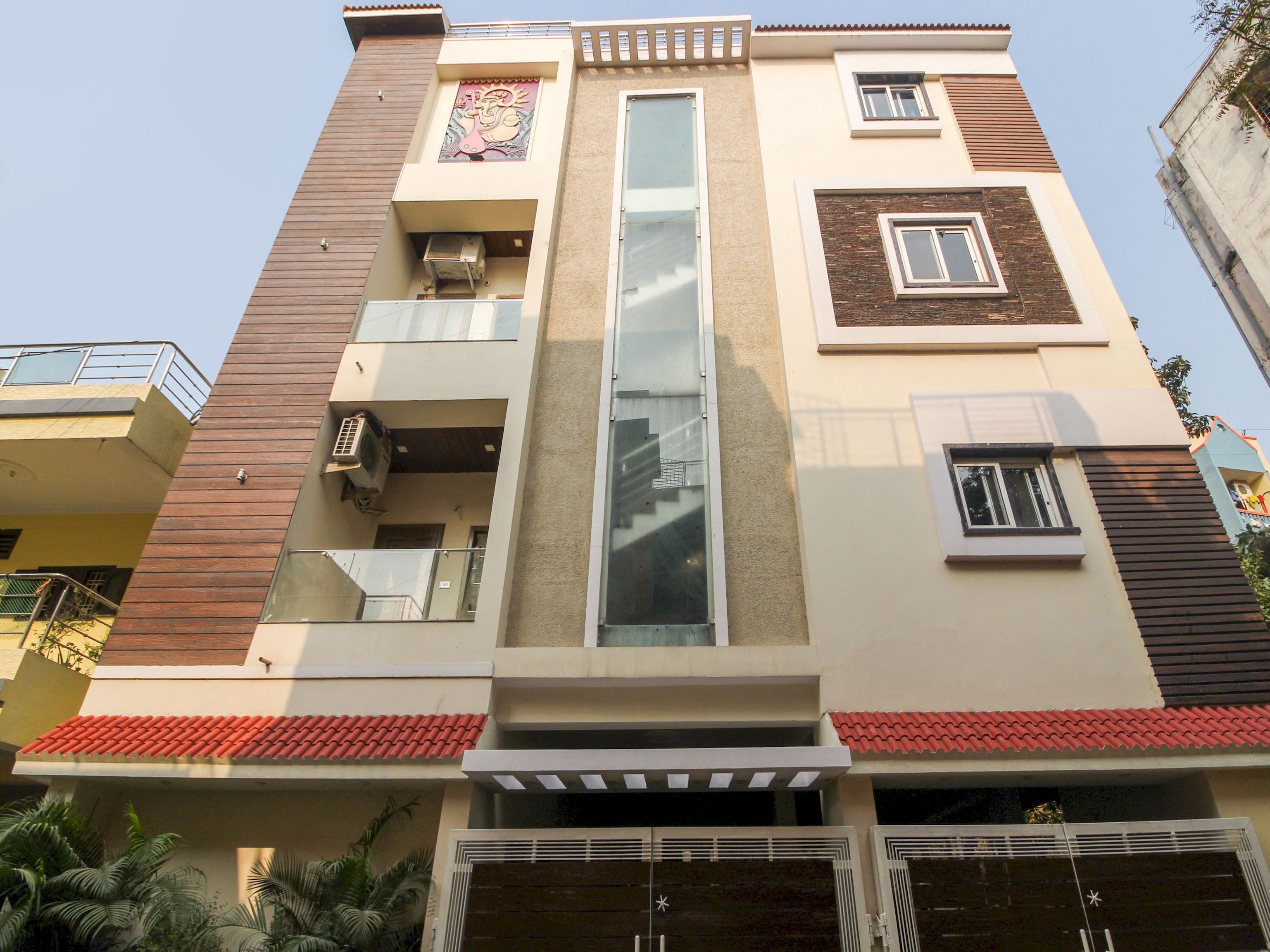 Un edificio residencial de varios pisos con balcones, fachada central de vidrio y techo de tejas rojas.