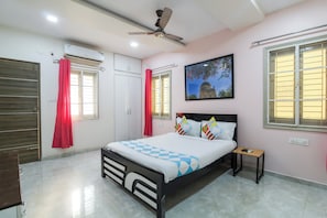 A bedroom with a bed, a nightstand, a ceiling fan, and a window with a view of a building. - Hotel O Home Dk Homes (Hyderabad)