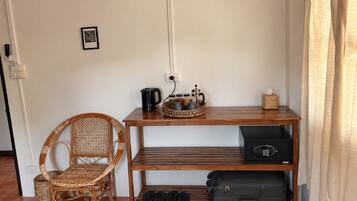 Une pièce comprenant une chaise en osier, une table en bois sur laquelle se trouve un plateau avec divers objets, une valise noire et un haut-parleur noir.