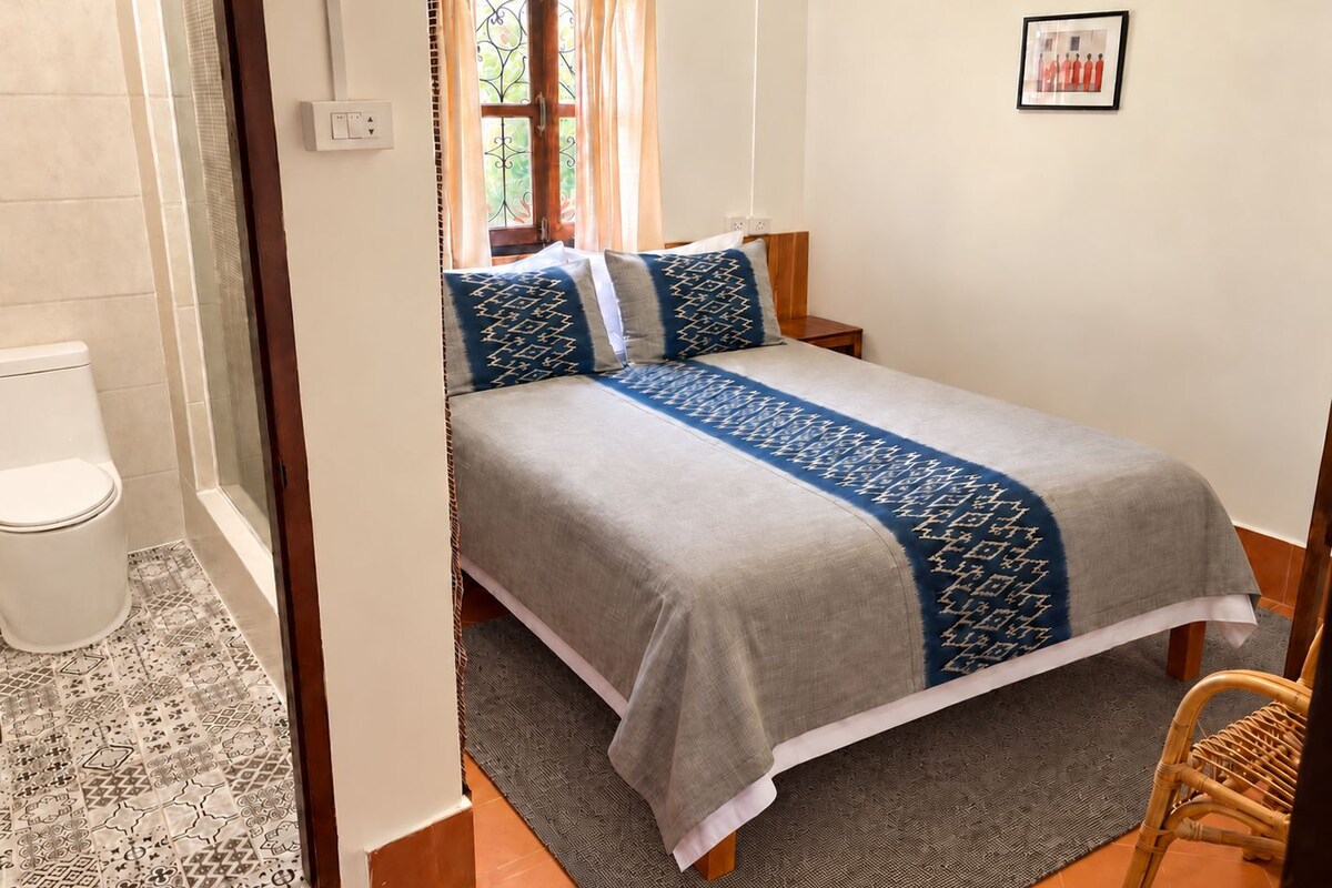 A bedroom with a bed, a nightstand, a chair, and a window with curtains.