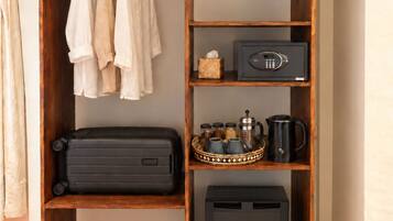 Une armoire en bois contenant des vêtements suspendus, un coffre-fort, un plateau avec des ustensiles de cuisine et une valise noire.