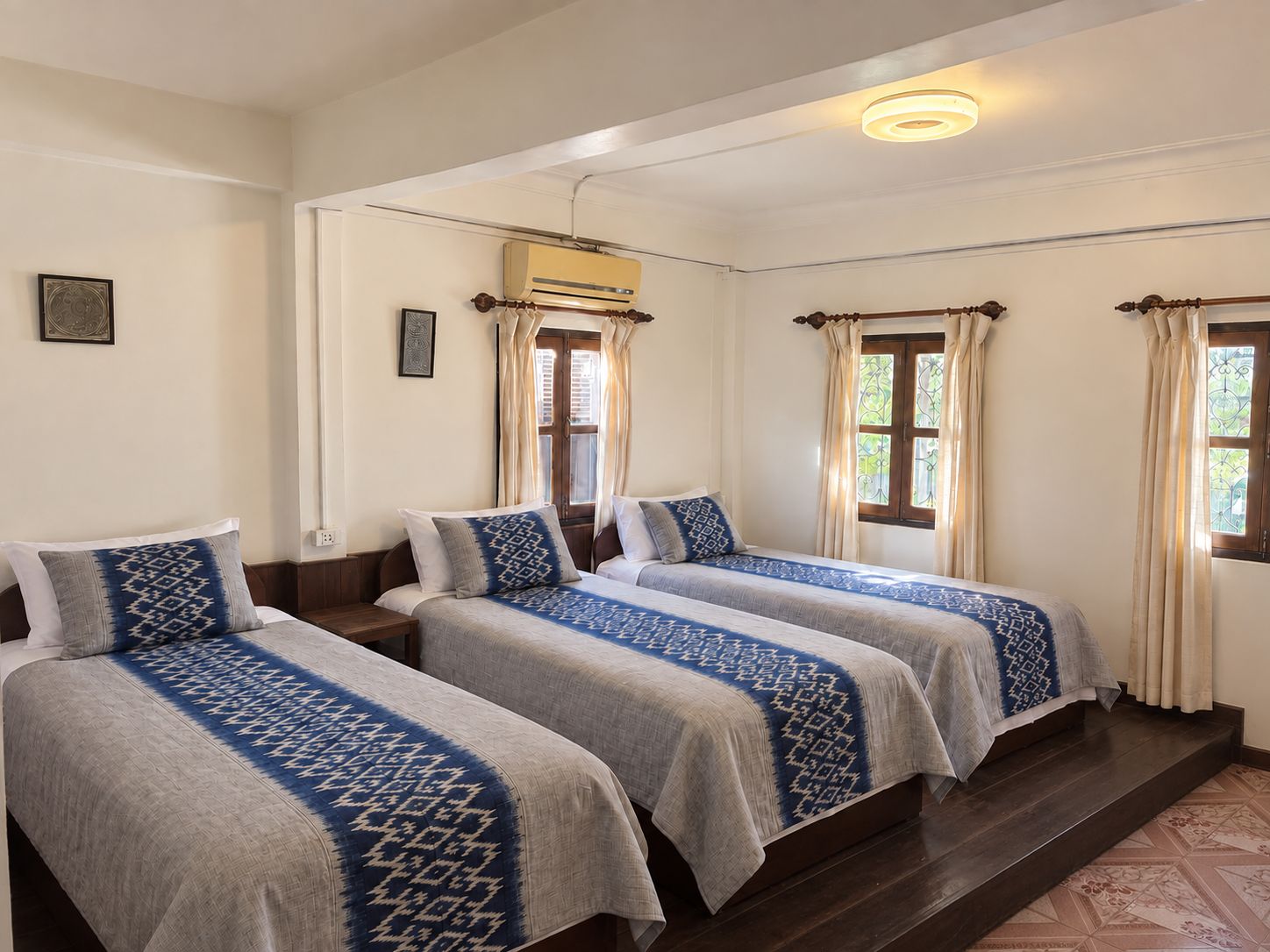 Ein Hotelzimmer mit zwei Betten, einem Deckenventilator, einer Klimaanlage und einem Vorhangfenster.