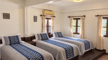 Habitación de hotel con dos camas, ventilador de techo, equipo de aire acondicionado y una ventana con cortinas.