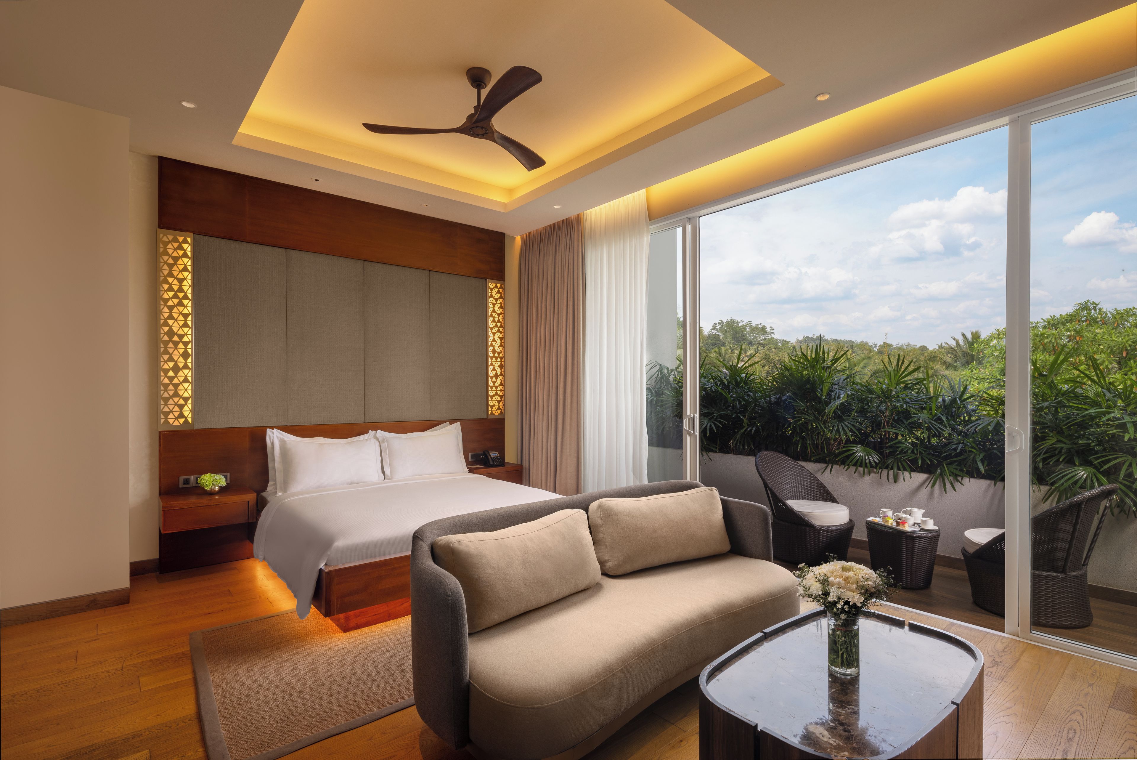 A modern hotel room with a bed, sofa, and a balcony with plants.
