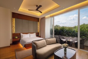 A modern hotel room with a bed, sofa, and a balcony with plants.