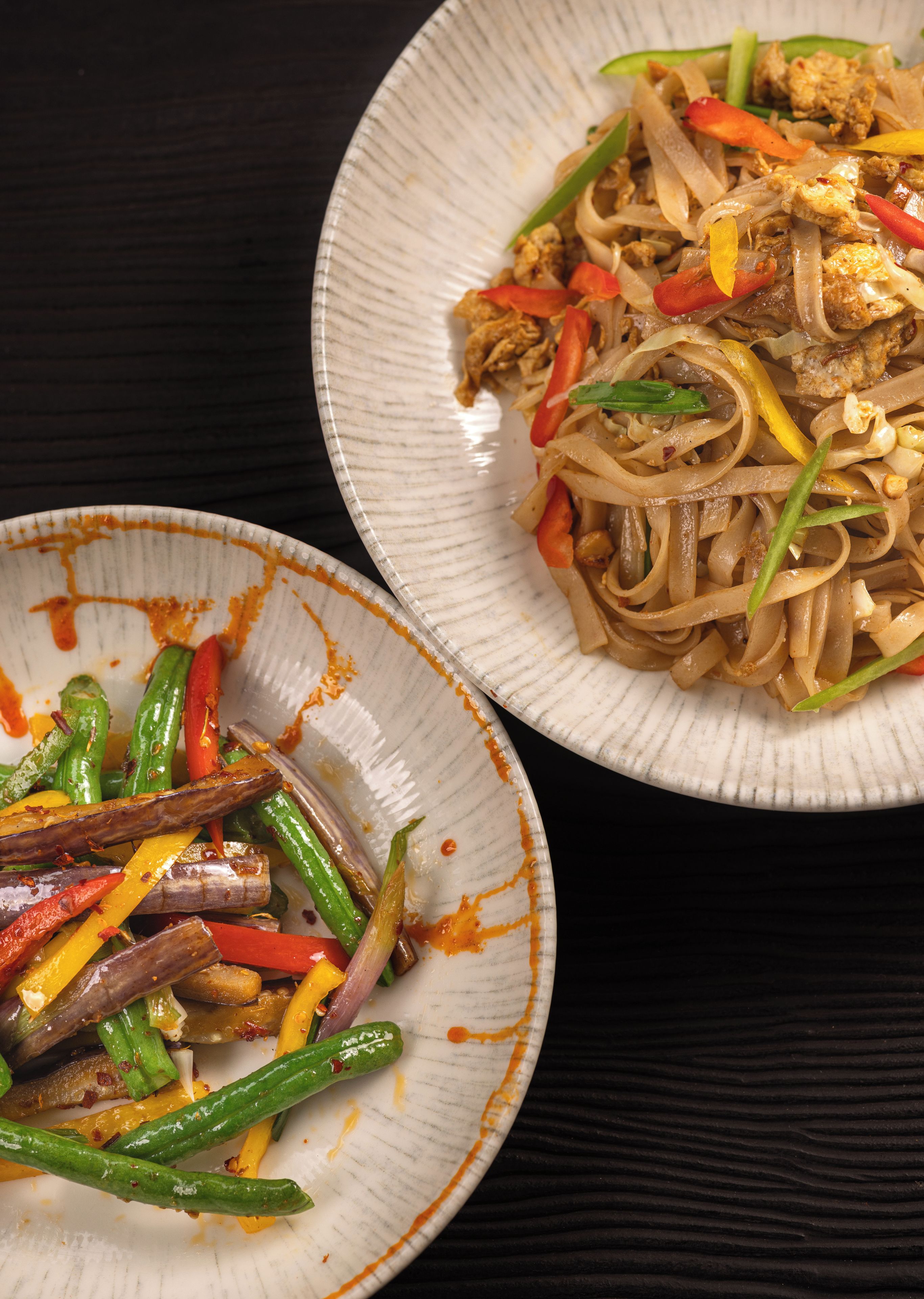 Two plates of stir-fried noodles with vegetables and meat, served on white plates with orange sauce stains.