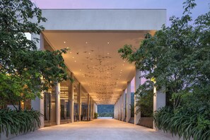 A modern building entrance with a glass facade, a central atrium, and hanging light fixtures.