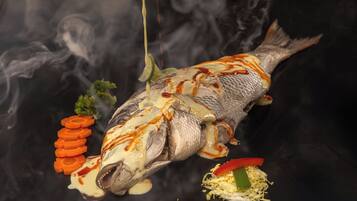 A whole fish with sauce and garnishes on a black surface.