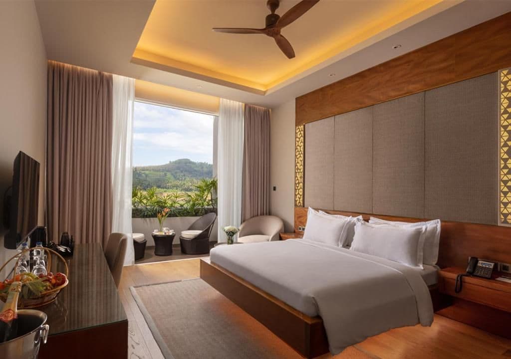A hotel room with a large bed, a desk with a chair, a television, and a view of the outdoors.