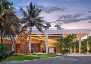 Un hotel moderno con una gran escultura de palmera en la entrada, un césped bien cuidado y un cielo despejado.