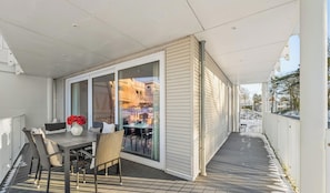 A covered outdoor seating area with a table and chairs, a vase with flowers, and a view of a building through glass doors. - Spacious Apartment with exceptional Sea View and Wellness Area! (Lübeck)