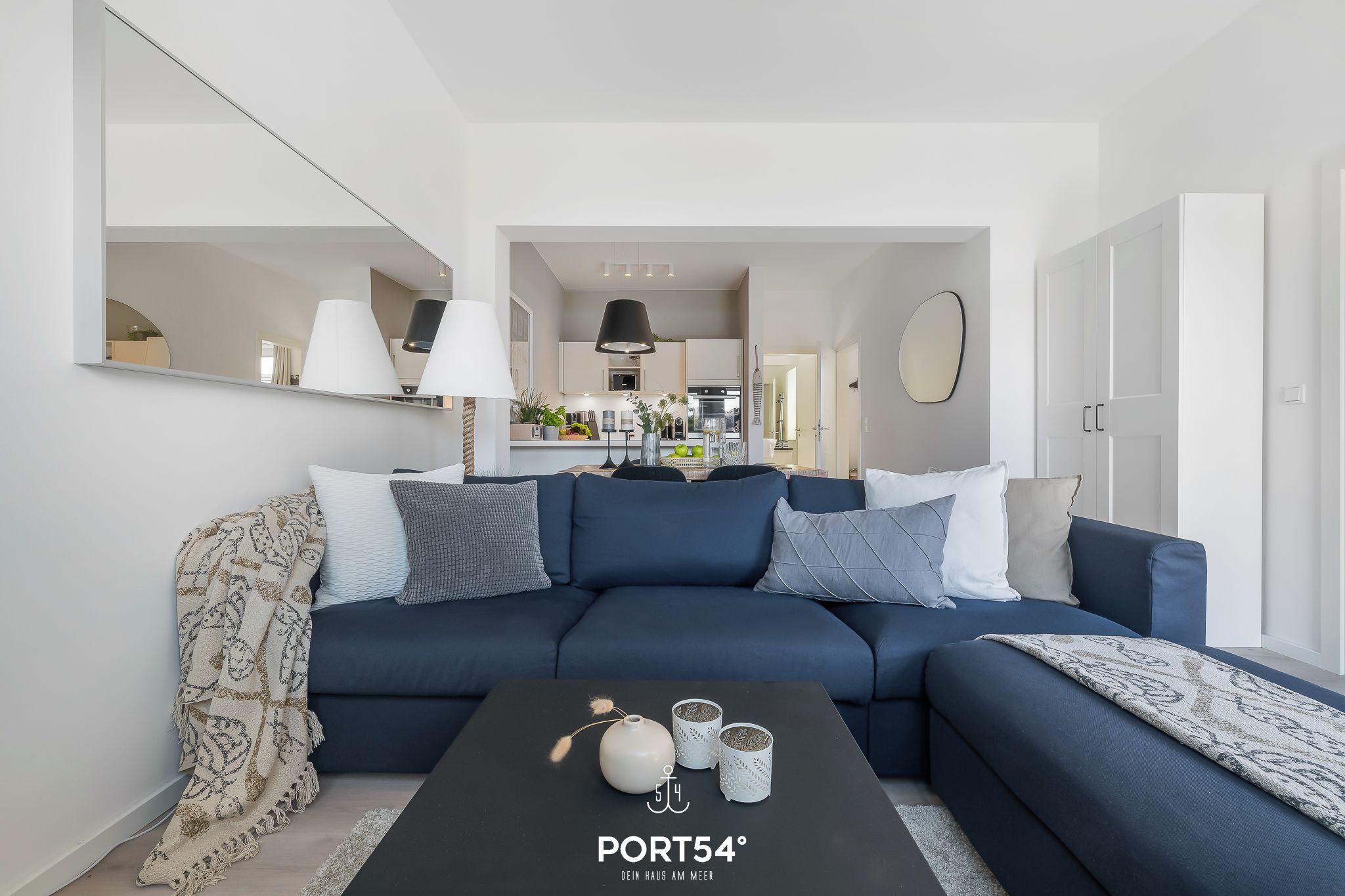 A modern living room with a dark blue sofa, a coffee table with decorative items, and a kitchen in the background.