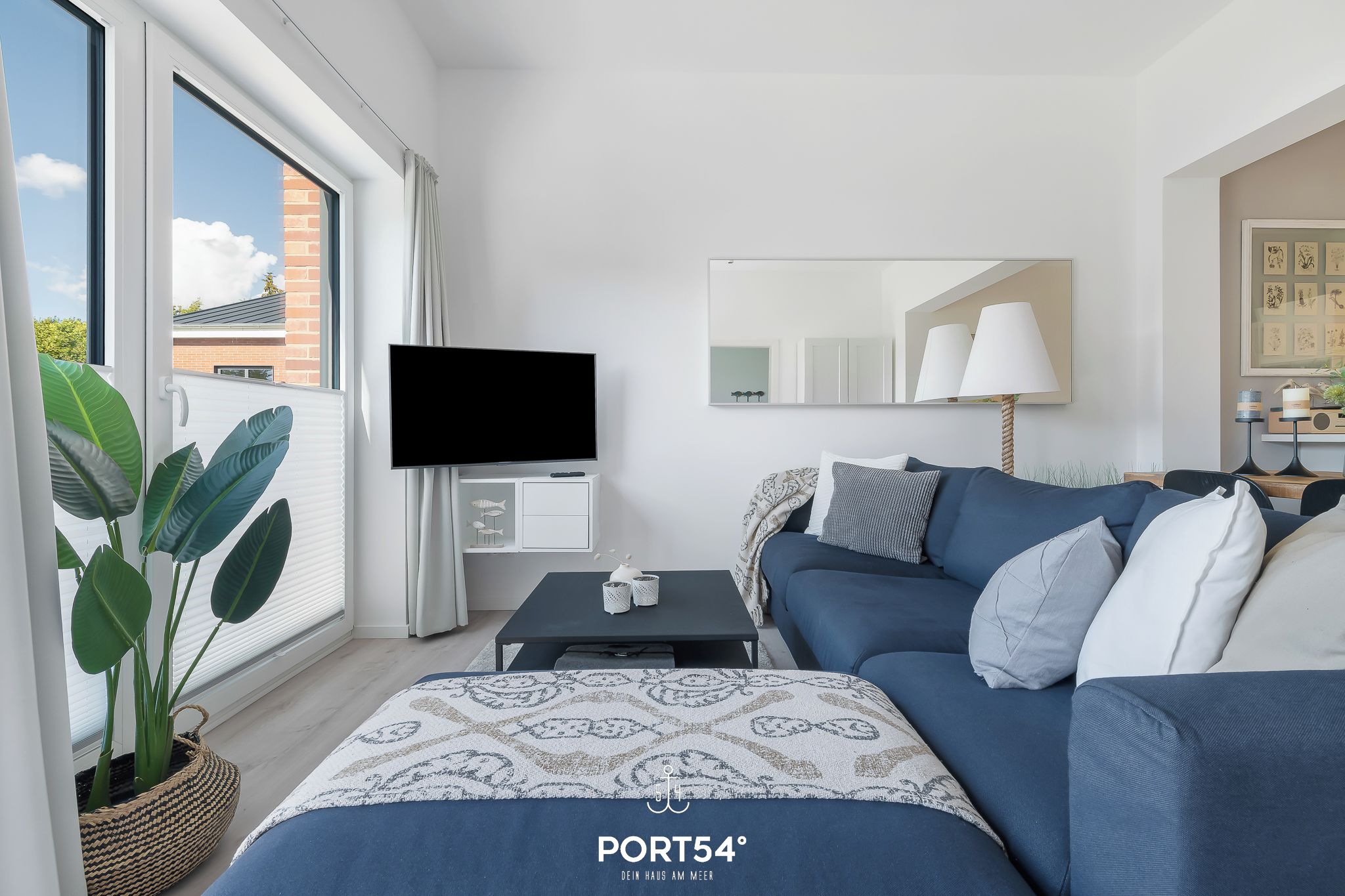 Ein modernes Wohnzimmer mit einer Couch, einem Flachbildfernseher, einem Couchtisch und einem großen Fenster mit Vorhängen.