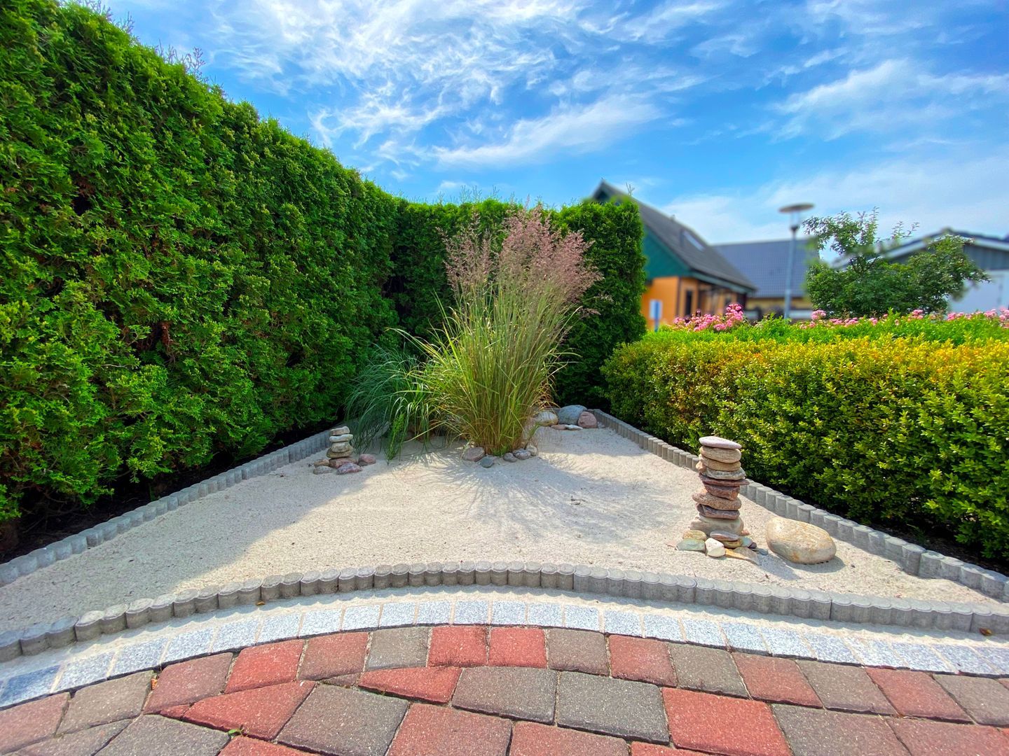 A landscaped garden with a curved pathway, neatly trimmed hedges, and a stack of stones.