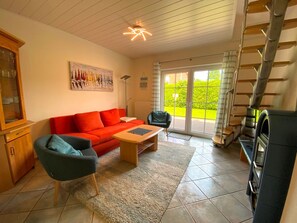 Ein Wohnzimmer mit einem roten Sofa, einem blauen Sessel, einem Holztisch und einem schwarzen Grill.