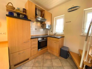 A compact kitchen with wooden cabinets, a built-in oven, a microwave, and a window with a view. - Friesenhaus for 4 – Baltic Sea Bliss for the Whole Family (Schönberg (Holstein))