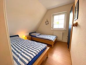 A small, triangular room with two single beds, a window, a radiator, and a door. - Friesenhaus for 4 – Baltic Sea Bliss for the Whole Family (Schönberg (Holstein))