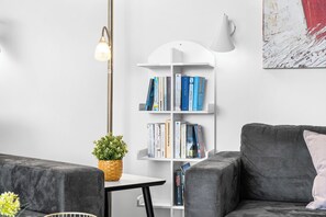 A modern living room with a grey sofa, a white bookshelf, and a floor lamp. - Spacious holiday apartment with luxury features and covered terrace near the Bal (Lübeck)