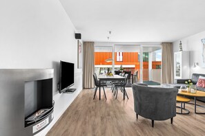 A modern living room with a flat-screen TV, a fireplace, and a dining area with a table and chairs. - Spacious holiday apartment with luxury features and covered terrace near the Bal (Lübeck)