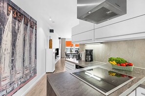 Una cuina moderna amb una illa central, un quadre gran a l'esquerra i una zona de menjador al fons.