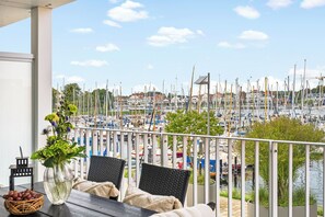 A balcony with a view of a marina, wicker furniture, a vase with flowers, and a basket of fruit. - Spacious holiday apartment with luxury features and covered terrace near the Bal (Lübeck)