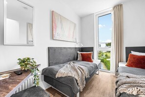 A modern bedroom with a large bed, a smaller bed, a desk, and a window with a view. - Spacious holiday apartment with luxury features and covered terrace near the Bal (Lübeck)