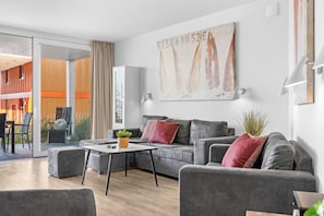 A modern living room with a grey sofa, a coffee table, and a large abstract painting on the wall. - Spacious holiday apartment with luxury features and covered terrace near the Bal (Lübeck)