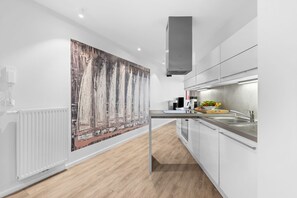 A modern kitchen with white cabinetry, a large wooden floor, and a large abstract painting on the wall. - Spacious holiday apartment with luxury features and covered terrace near the Bal (Lübeck)