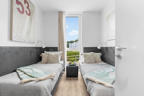 A modern bedroom with two beds, a small table, and a view of greenery outside. - Spacious holiday apartment with luxury features and covered terrace near the Bal (Lübeck)