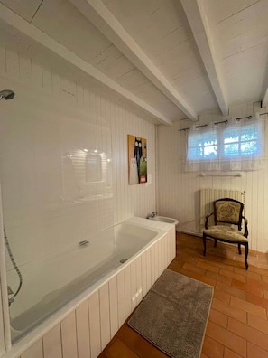 Ein Badezimmer mit einer großen Badewanne, einem Sessel und einem Fenster mit Vorhängen.