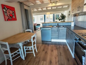 Moderni keittiö, jossa on puinen ruokapöytä, valkoiset tuolit ja ruostumattomasta teräksestä valmistetut kodinkoneet.