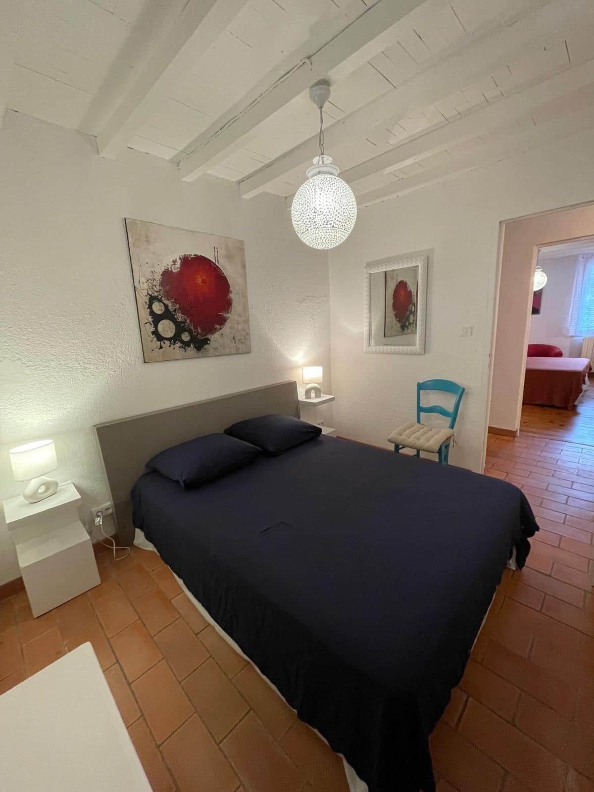 A bedroom with a bed, bedside tables, a chair, and artwork on the walls.