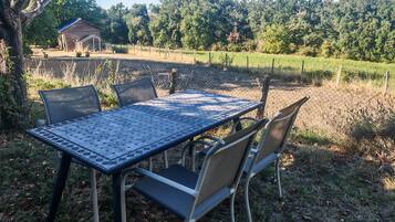 An outdoor table and chairs set in a grassy area with a fence and trees in the background.